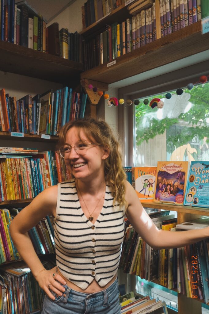 Rea smiling in a bookshop full of picture books