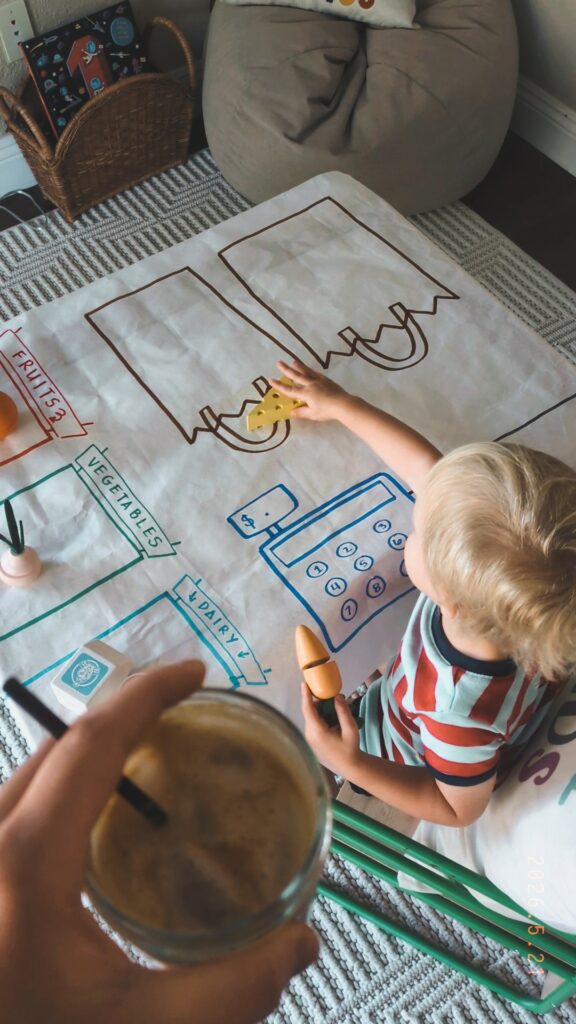 Toddler boy playing with a butcher paper grocery checkout