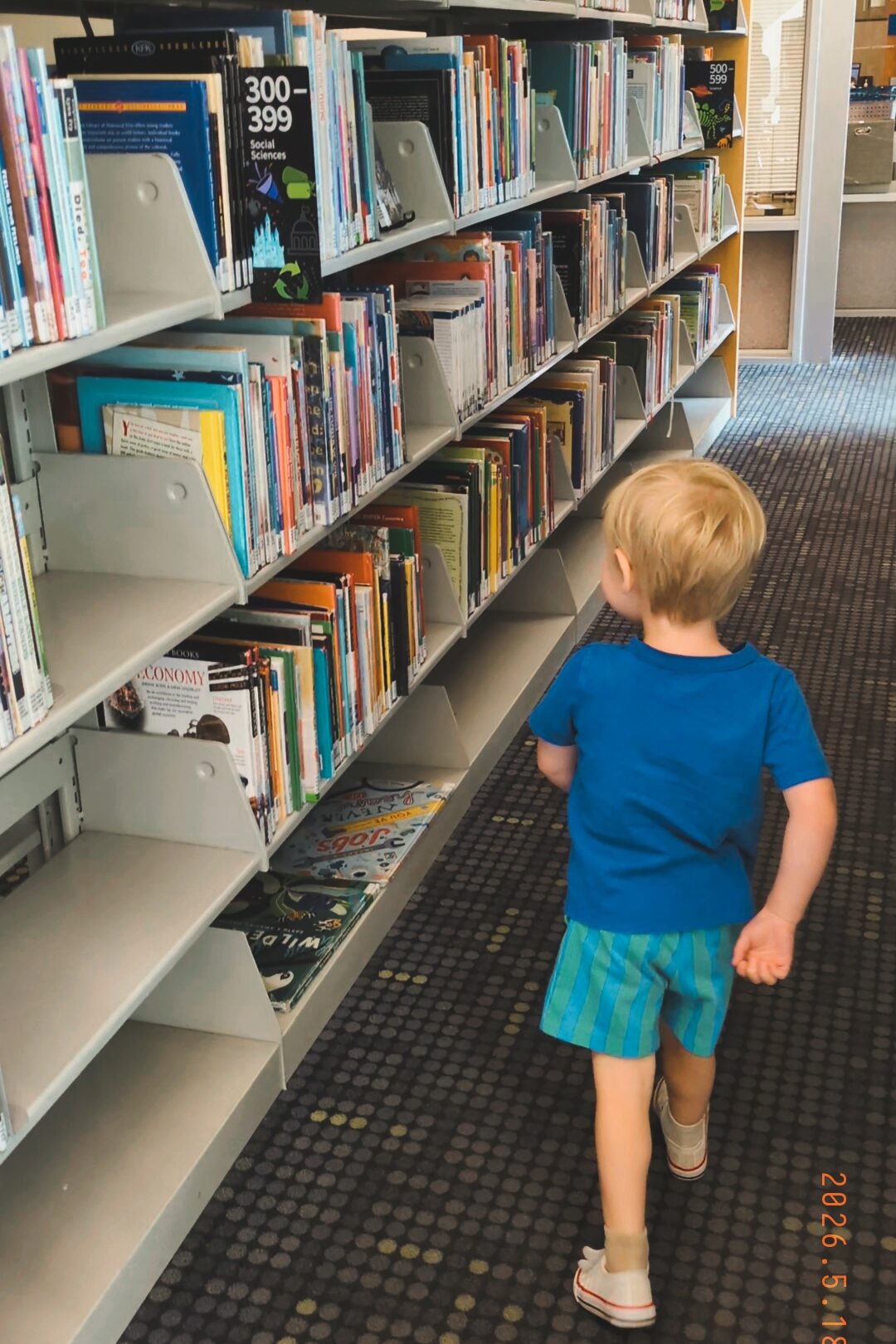 boy walking around library surrounded by books.